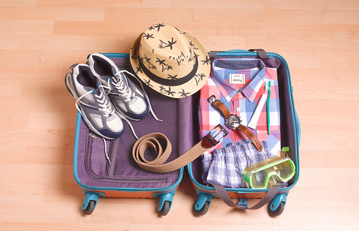 una-valija-de-viaje-pequeña-abierta-con-zapatillas,-un-sombrero,-una-correa,-una-camisa,-un-reloj-y-lentes-de-buceo-sobre-la-valija.
